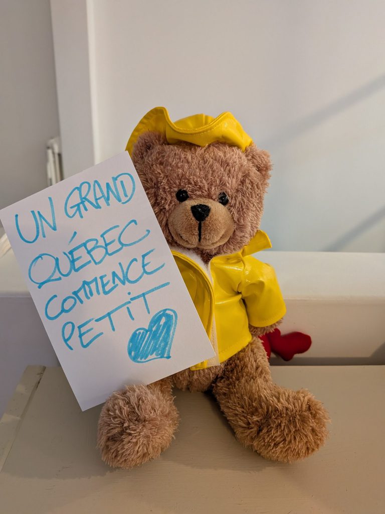 Teddy bear in a yellow raincoat holding a sign reading “Un grand Québec commence petit” (Quebec’s future starts with its youngest)